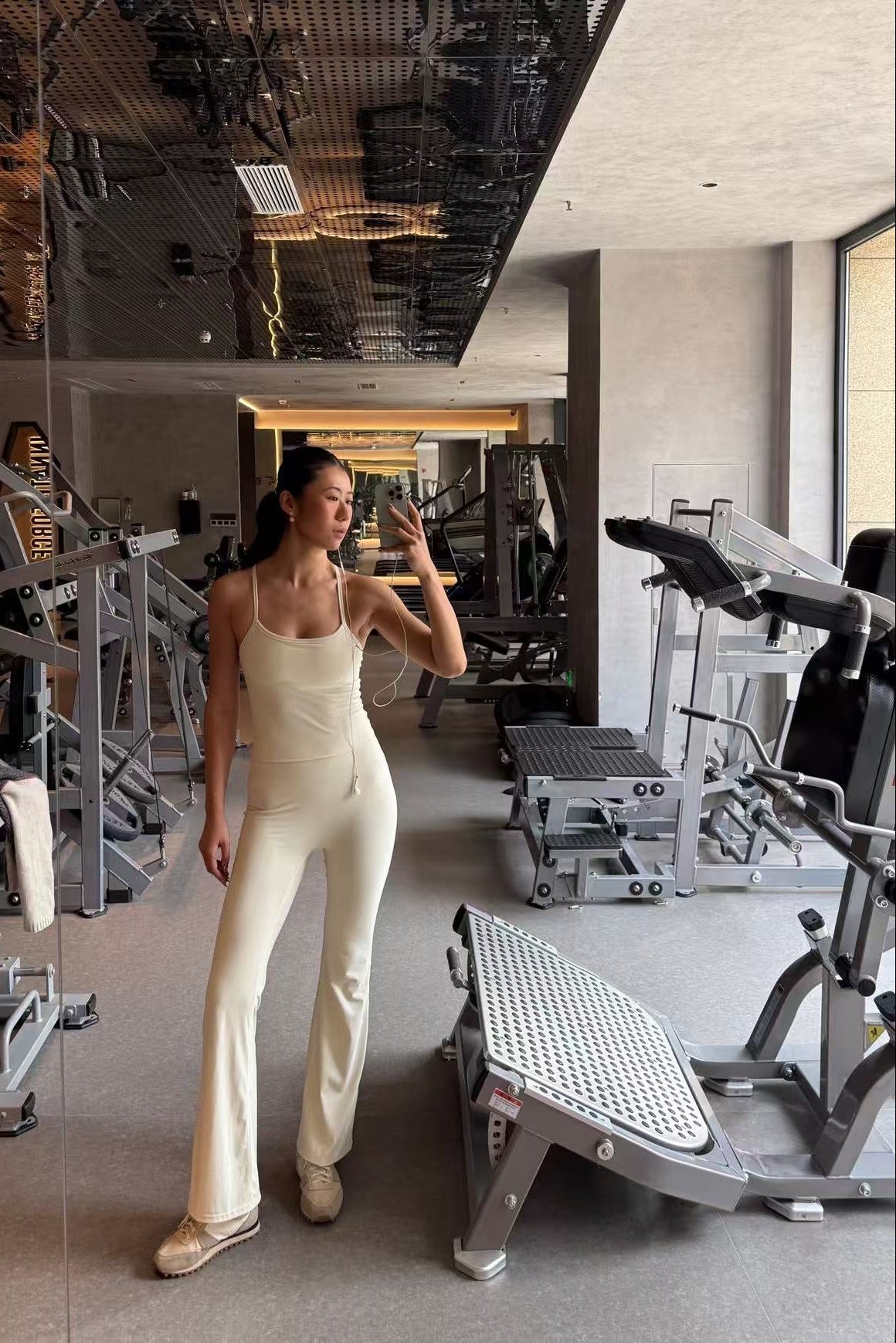 Woman taking a selfie in a modern gym with exercise equipment wearing a bone shade set.
